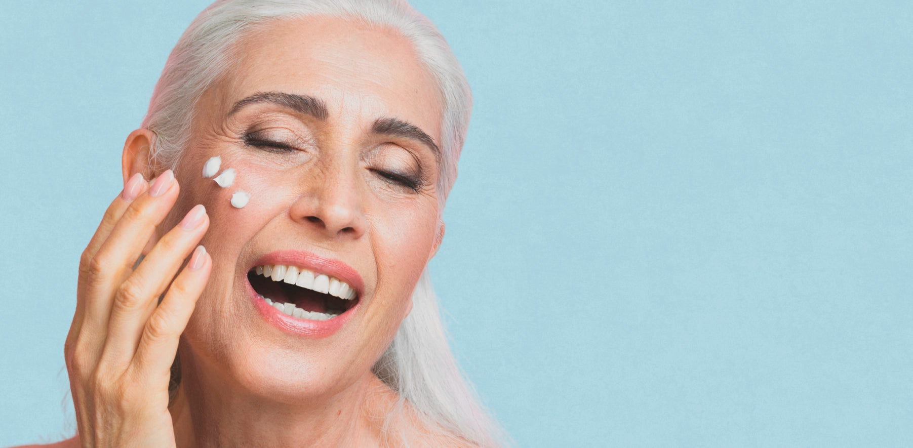 Mujer mayor sonriendo aplicándose crema en la cara