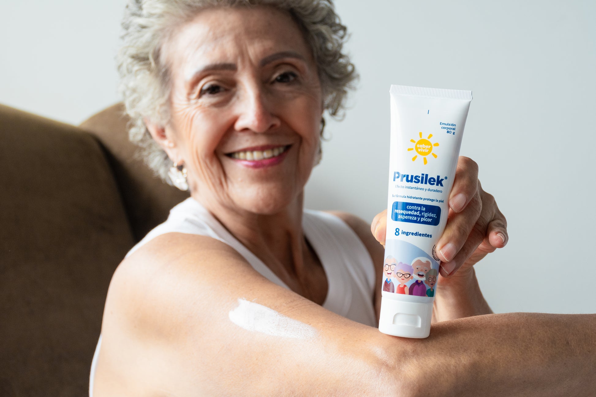 Mujer mayor sonriendo con crema para a rasquiña en la piel, untada sobre un brazo.