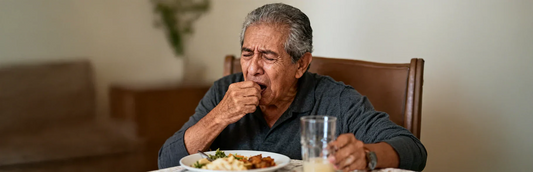 Hombre mayor tiene molestias para tragar sentado en la mesa