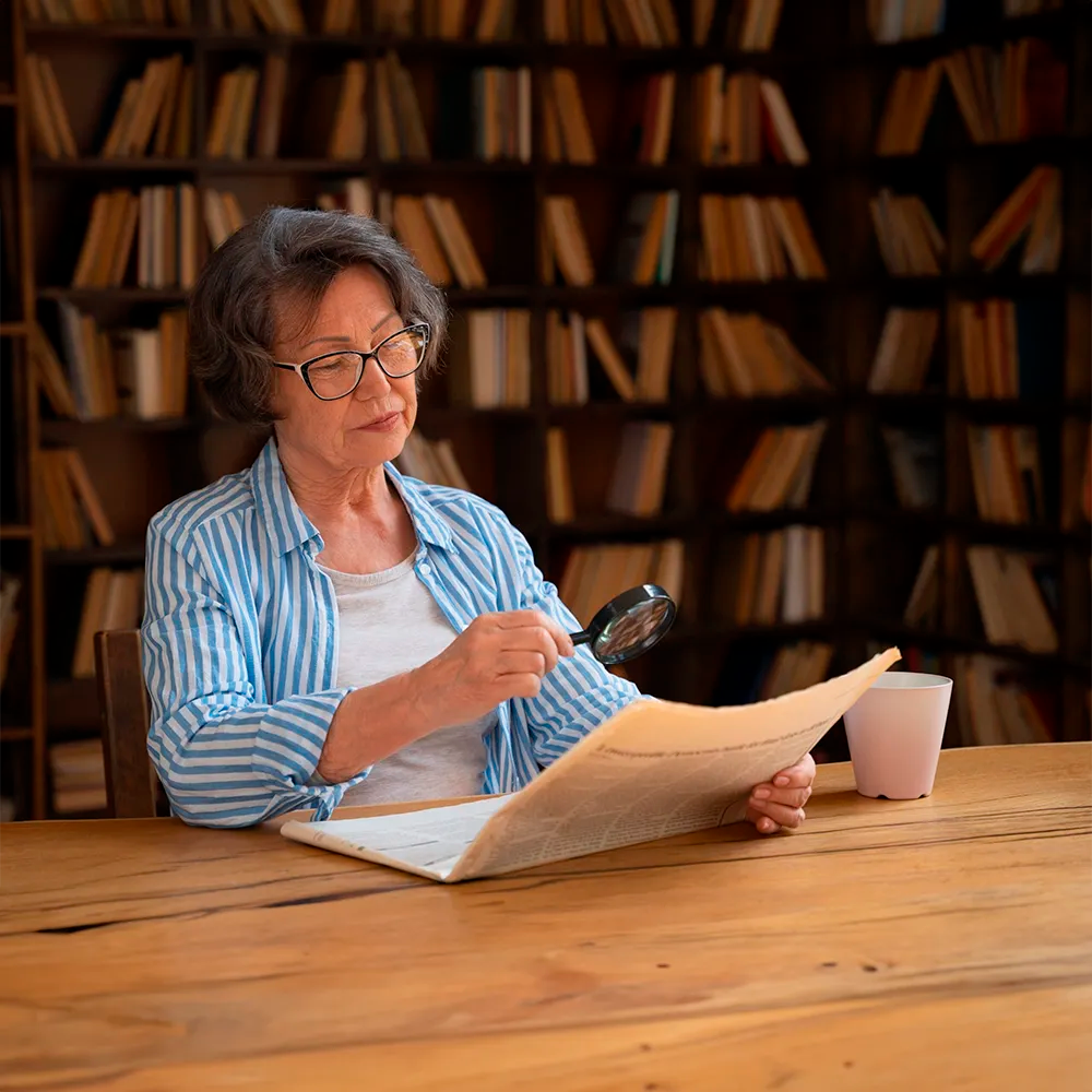 Mujer mayor leyendo con una lupa en una biblioteca