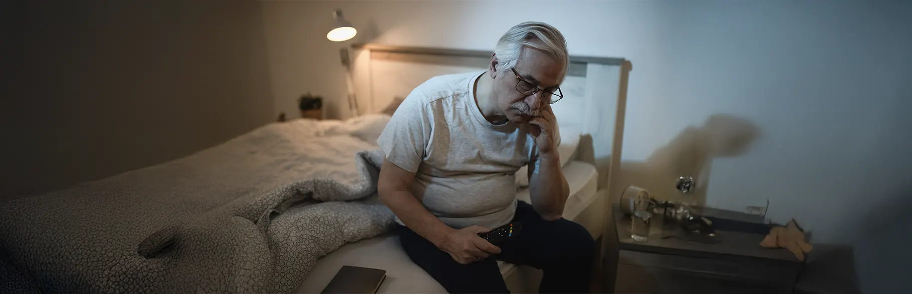 Hombre mayor sentado en la cama en la noche con cara de preocupación 