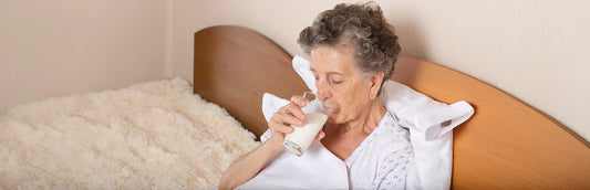 Mujer mayor en cama tomando un batido 